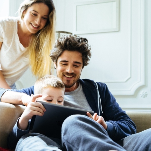 Cheerful Young Family Looking At Digital Tablet Together