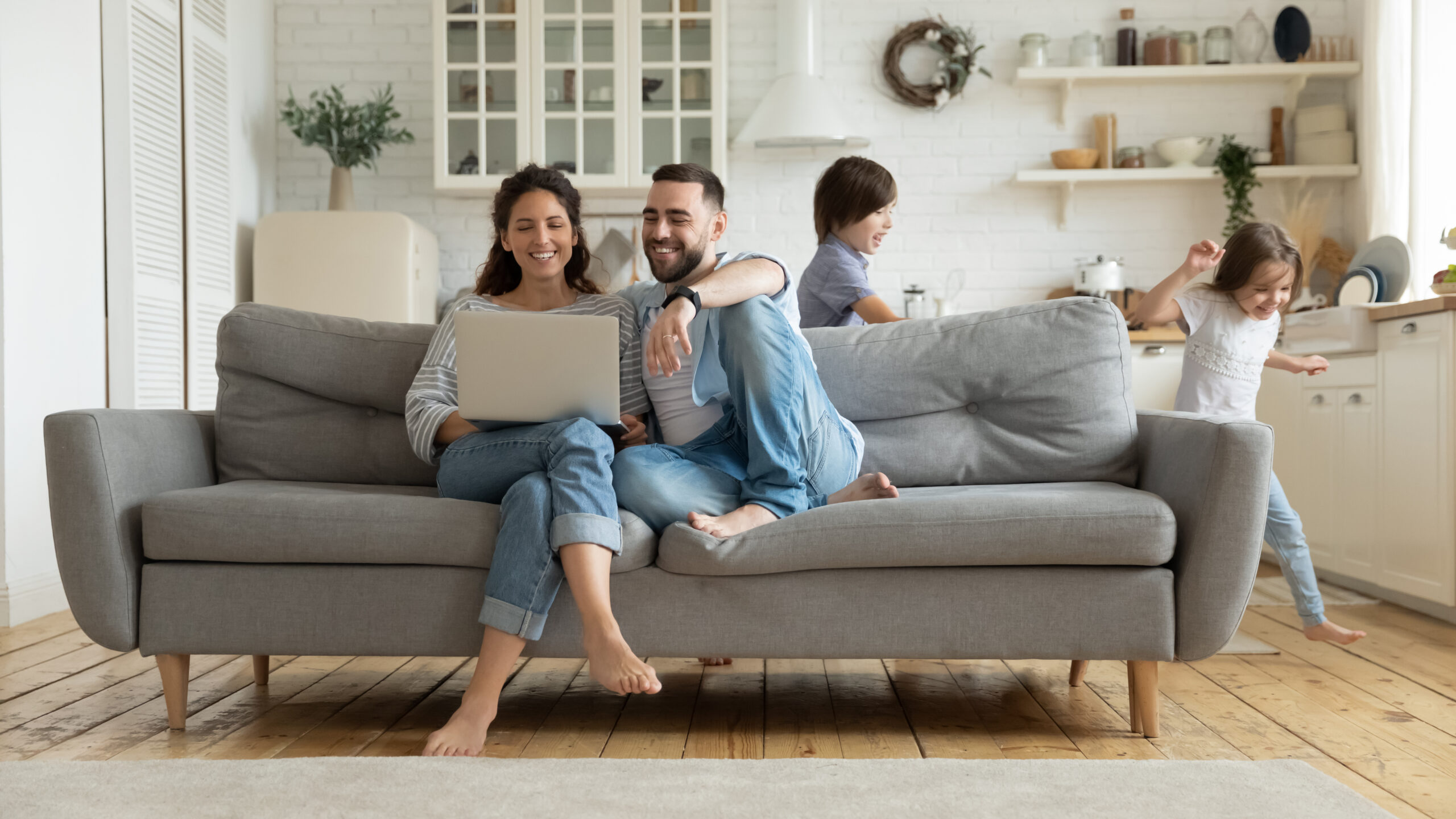 While active kids running parents resting on sofa using laptop